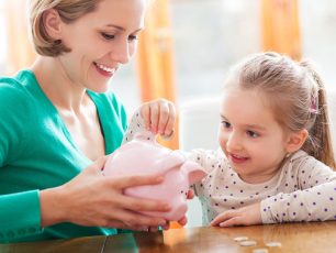 a woman and a little girl putting coins into a piggy bank.