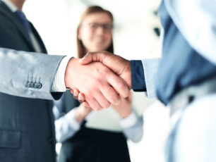 two business people shaking hands in front of a woman.