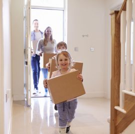a little girl carrying a cardboard box down a hallway.