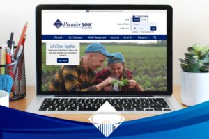 New Premier Bank .bank website on computer screen with coffee cup, mobile phone, and plant nearby